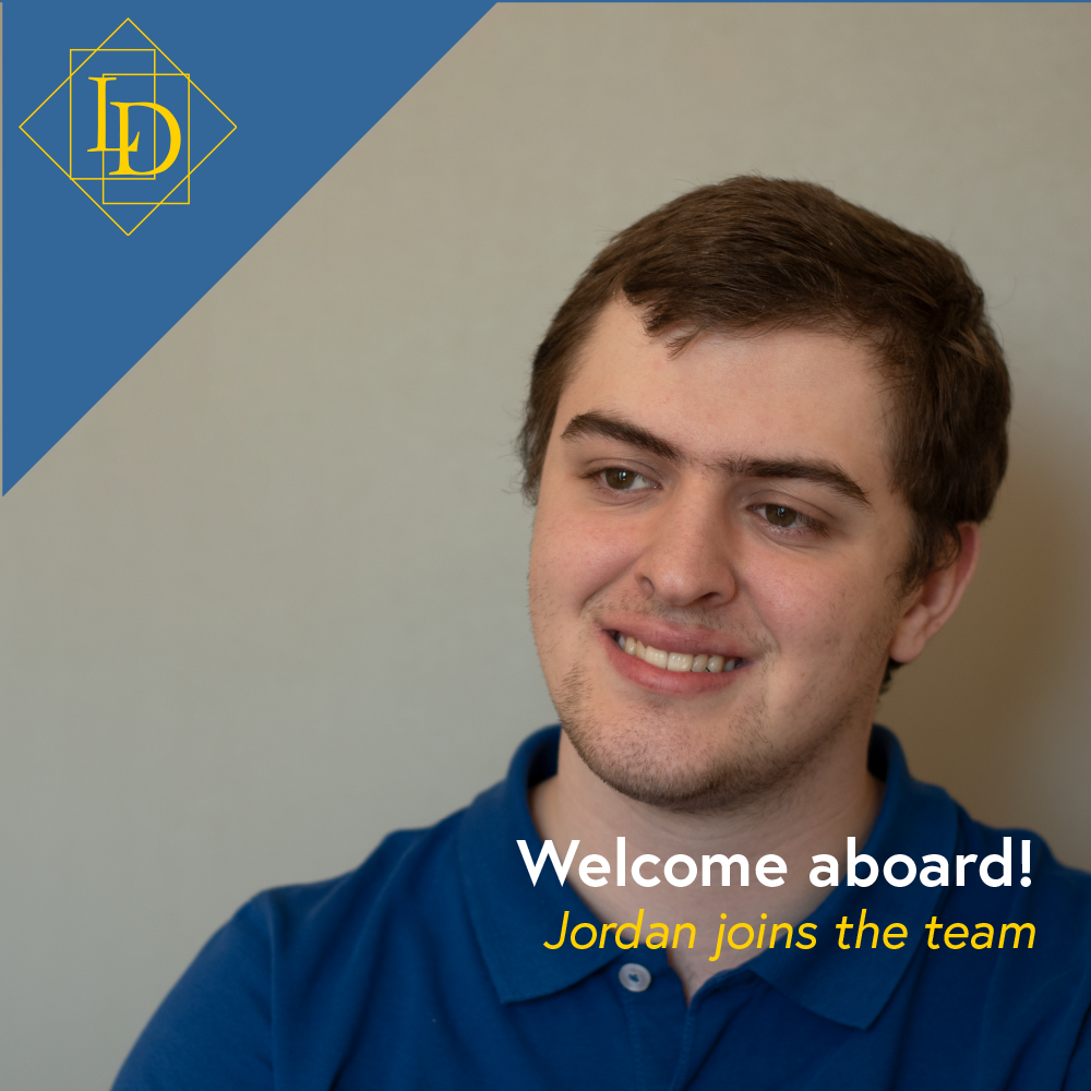 It's a photo of Jordan! He is looking from the right toward the left. His head is tilted to the viewers right and has a slight smile. In the bottom right corner is the title of the article, "Our team grows!". In the top left corner is the Logical Developments logo in gold on a blue background. The logo is a diamond with the letters L and D inside of it. The letters are offset from each other vertically while also overlapping horizontally. The each sit inside of their own rectangle.